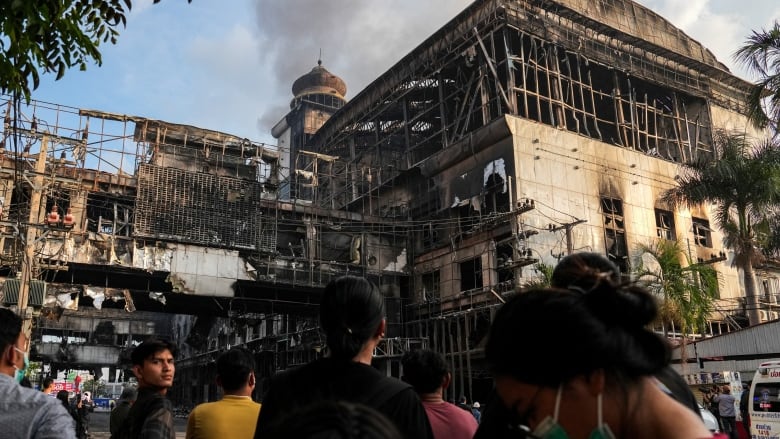 A crowd of people look at the remains of a charred building.