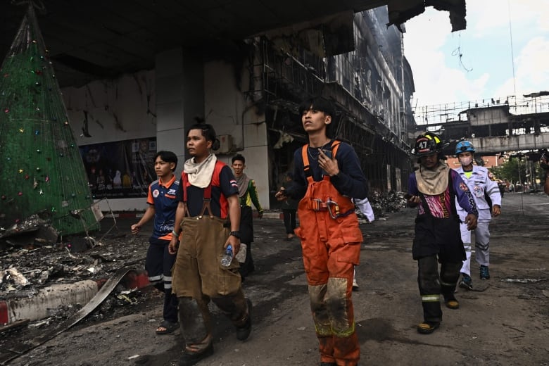 People in firefighting and paramedic gear walk through a burned part of a building complex.